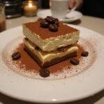 Final presentation of classic tiramisu cheesecake on a plate, showcasing its rich layers and cocoa for a delightful dessert experience.