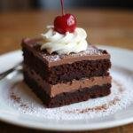 Indulgent Ghirardelli cake slice served with whipped cream and cherry, an irresistible treat for dessert lovers.
