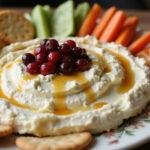 Final presentation of the whipped feta dip with honey and cranberries. Delightful display with vegetables and crackers, perfect for parties.