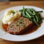 Serving a delicious slice of classic meatloaf alongside mashed potatoes and green beans, perfect for a family meal.