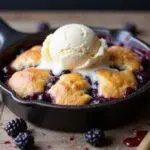 Delicious blackberry cobbler with cake mix served with ice cream, showcasing the final result of the baking process in a beautifully styled kitchen setting.