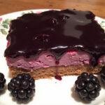 Completed Forbidden Forest Blackberry Cheesecake Bars with a Midnight Glaze, showcasing a luscious slice decorated with a midnight glaze and fresh berries on a decorative plate.