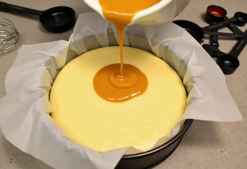 Pour the cheesecake filling over the crust for Golden Snitch Butterbeer Cheesecake Bars, adding a swirl of butterscotch.