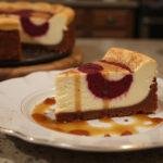 Final presentation of Gryffindor Spiced Caramel Cheesecake with Red Velvet Swirl on a dessert plate with caramel and cinnamon garnishes.