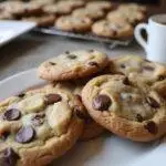 Freshly baked Jacques Torres chocolate chip cookies on a cooling rack with a cup of coffee.