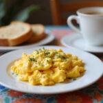 Garnished fluffy scrambled eggs in air fryer presented on a plate, perfect for a delicious breakfast, alongside toast and coffee.