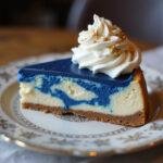 Final presentation of Ravenclaw Starry Night Butterbeer Cheesecake slice with blue velvet swirl, garnished with whipped cream and edible glitter, elegant plating.
