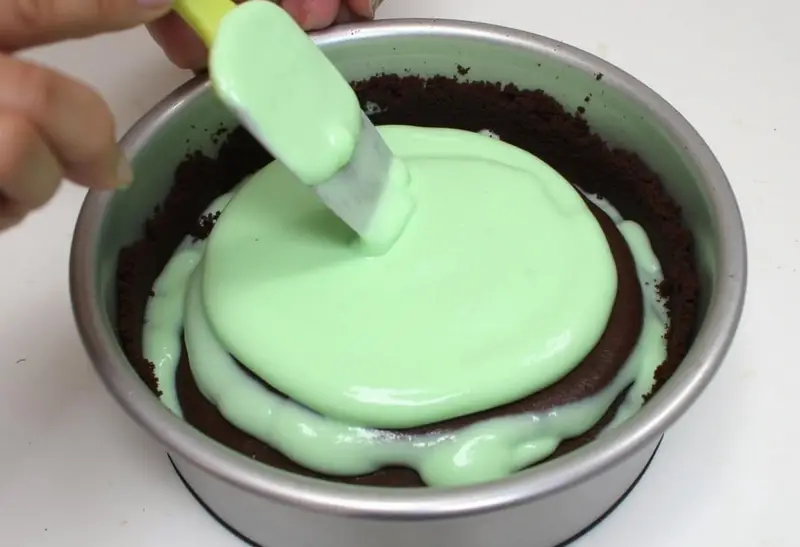 Pouring mint cheesecake filling into chocolate crust for Slytherin Mint Cheesecake.