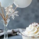 A beautifully decorated baby shower setup featuring a pastel color palette with snowflake motifs, adorable baby-themed table decorations, elegant floral arrangements, and a cake adorned with winter-themed decorations. The scene includes guests happily mingling, with soft fairy lights creating a warm, inviting glow.