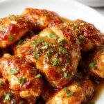 A plate of baked crunchy hot honey chicken garnished with fresh herbs, served alongside a side of vegetables and drizzled with honey and chili sauce.