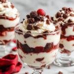 A festive Christmas Black Forest Trifle layered with whipped cream, cherries, chocolate shavings, and sponge cake in a glass bowl