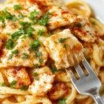 A vibrant plate of chicken linguine featuring tender sliced chicken breast atop al dente linguine, coated in a rich, golden cowboy butter sauce, garnished with chopped parsley and red pepper flakes, with a side of lemon wedges and fresh herbs on a rustic wooden table.