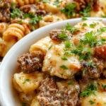 A close-up of a golden-brown baked pasta dish topped with shredded cheese and drizzled with a glossy honey Buffalo sauce, garnished with chopped herbs on a rustic plate.