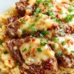A vibrant plate featuring golden-brown juicy steak strips nestled atop a bed of creamy white queso rice, garnished with fresh herbs and served on a rustic ceramic plate with a glossy finish. The rice appears fluffy and coated with a cheesy sauce, while the steak strips are tender and glistening, creating an inviting and hearty presentation.