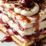 A close-up of a beautifully layered tiramisu in a glass dish, showing creamy mascarpone layers dusted with cocoa powder and topped with vibrant cherry halves and a drizzle of amaretto syrup. The dessert has a rich, velvety texture with distinct layers of ladyfingers soaked in coffee and laced with amaretto, stunningly presented with elegant garnishes.