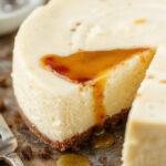 A slice of decadent vanilla bean brown butter cheesecake on a elegant white plate, topped with a vanilla bean pod and a drizzle of caramel sauce. The creamy, smooth interior reveals a rich, golden-brown crust, with a glossy surface highlighting the vanilla specks and luscious texture.