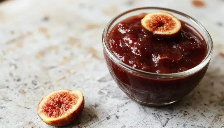 A glass jar filled with vibrant amber-colored fig jam, surrounded by fresh, ripe figs and sprigs of thyme on a rustic wooden surface, with a spread of jam and slices of bread beside it.