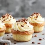 A batch of fluffy Japanese Cotton Cheesecake cupcakes displayed on a white plate, showcasing their delicate, airy texture with a golden-brown top. The cupcakes are topped with a dusting of powdered sugar, and their soft, cloud-like interior is slightly visible through a cut-open slice. The background is softly blurred, emphasizing the lightness and elegance of the desserts.