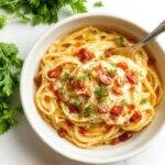 A close-up of a bowl of garlic butter pasta, featuring golden spaghetti coated in rich, glossy garlic butter sauce, garnished with chopped parsley and grated Parmesan, with a sprinkle of red pepper flakes for color contrast, presented on a rustic wooden table.