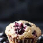 A tray of moist, fluffy healthy blueberry protein muffins garnished with fresh blueberries and sprinkled with a light glaze.