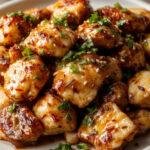 A plate ofHealthy Sesame Chicken garnished with sesame seeds and green onions, served with steamed rice and fresh vegetables.