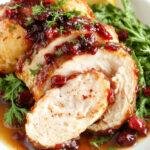 A perfectly cooked turkey breast glazed with a vibrant orange and cranberry sauce, garnished with fresh herbs. The meat has a golden-brown, crispy skin with a glossy, colorful glaze, served sliced on a platter with cranberries and orange slices for garnish.