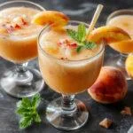 A clear glass filled with vibrant orange-peach colored slurpee topped with a slice of fresh peach and a sprig of mint, condensation on the glass, set on a summer-themed background with scattered peach slices and ice cubes.