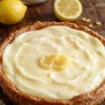 A slice of honey lemon chiffon pie on a elegant white plate, showcasing a fluffy, golden-yellow filling with a light, airy texture. The crust is crispy and golden brown, with a drizzle of honey and a twist of lemon zest on top garnished with fresh lemon slices and mint leaves. The background features a rustic wooden table and a cheerful summer setting.