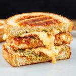 A close-up of a crispy beef ranch chicken melt sandwich showing melted cheese, crispy breading, and fresh toppings, served on a toasted bun.