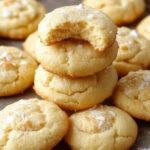 A close-up of a stack of golden-brown lemon coconut cheesecake cookies on a rustic wooden plate, garnished with shredded coconut and lemon zest, with a light drizzle of lemon glaze on top, showcasing their chewy texture and bright citrus appeal.