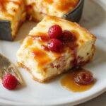 A golden-brown Basque cheesecake with a slightly caramelized crust, sliced to reveal its creamy, slightly jiggly interior, presented on a rustic wooden surface with a small plate and a silver fork nearby.