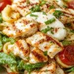 A vibrant layered grilled chicken caprese pasta salad with colorful cherry tomatoes, fresh basil, mozzarella, and grilled chicken slices arranged in a clear glass bowl.