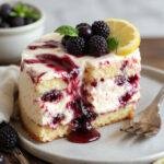 A slice of Lemon Blueberry Shortbread Mousse Cake showcasing layers of yellow lemon mousse, vibrant blueberries, and golden shortbread crust garnished with fresh berries and lemon zest.