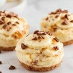 Mini banana cream pies topped with whipped cream and sliced bananas on a decorative plate.