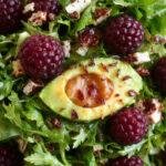 A vibrant plate of blackberry, avocado, and arugula salad garnished with fresh herbs and a light vinaigrette, perfect for summer.