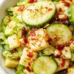 A vibrant plate of green cabbage and cucumber salad garnished with fresh herbs, showcasing crisp textures and bright colors