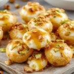 Close-up of bite-sized ricotta honey pistachio treats neatly arranged on a white plate. The bites are topped with chopped pistachios and drizzled with honey, showcasing a golden hue with hints of green from the pistachios and creamy white ricotta base. The textures look smooth and crumbly with a glossy honey glaze.