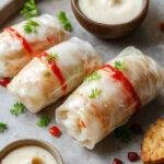 A vibrant plate of sweet summer rolls showcasing translucent rice paper wrapped around colorful fresh fruits and herbs, resting on a rustic wooden surface, with a bowl of creamy coconut rice pudding and a drizzle of sweet sauce in the background.