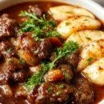 A steaming bowl of French Red Wine Beef Stew topped with fresh herbs, showcasing tender beef chunks, carrots, potatoes, and a rich, savory sauce