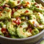 A vibrant avocado salad featuring sliced ripe avocados, cherry tomatoes, red onions, fresh herbs, and a light vinaigrette