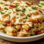 A golden-brown casserole topped with bubbling melted cheese and crispy edges, garnished with chopped green herbs. The dish showcases a creamy, cheesy layer with bits of tender chicken and rice, arranged in a rustic ceramic baking dish.