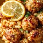 A vibrant plate featuring tender Greek chicken meatballs nestled atop a bed of glossy lemon-infused orzo pasta. The dish is garnished with fresh herbs, lemon wedges, and a drizzle of olive oil, creating a colorful and inviting presentation. The background includes rustic Mediterranean tableware, highlighting the bright yellow of the orzo and the golden-brown meatballs.