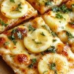 A vibrant lemon pizza topped with fresh lemon slices, basil leaves, and a golden crust on a rustic wooden table.