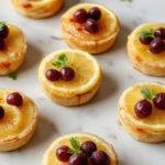A batch of vibrant mini vegan lemon tarts with bright yellow filling topped with fresh mint leaves on a white plate.