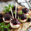 Vivid purple blackberry cheesecake pops on decorative sticks, set against a rustic wooden platter with fresh blackberries and mint garnish, showcasing smooth creamy texture with glistening berry glaze and crunchy sticks, styled in natural daylight for an inviting, homemade feel.