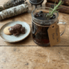 A vibrant glass filled with dark cola infused with magical herbs and glowing garnishes, styled on an aged wooden table with mystical lighting, featuring Harry Potter-themed props like a wand and a parchment scroll.