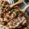 Golden-brown seared pork chops nestled in a rich, caramelized onion and mushroom gravy on a white ceramic plate, garnished with fresh parsley, resting on a clean wooden cutting board with soft natural lighting and shallow depth of field.