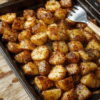 Gold-brown, crispy-edged roasted potatoes on a rustic baking sheet, drizzled with olive oil and fresh rosemary sprigs, with halved garlic cloves and lemon zest scattered nearby, soft shadows, natural daylight, shallow depth of field.