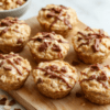 A close-up of creamy peanut butter oat cups set on a light marble countertop. The cups show a glossy peanut butter filling, oats visible, and a few chocolate chips sprinkled on top. They are arranged on parchment paper with a drizzle of honey and a rustic wooden background for a cozy, wholesome vibe.