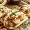 Golden-crusted sheet pan chicken bites tucked into warm pita pockets with crisp vegetables, tzatziki, and fresh parsley arranged on a rustic wooden board.